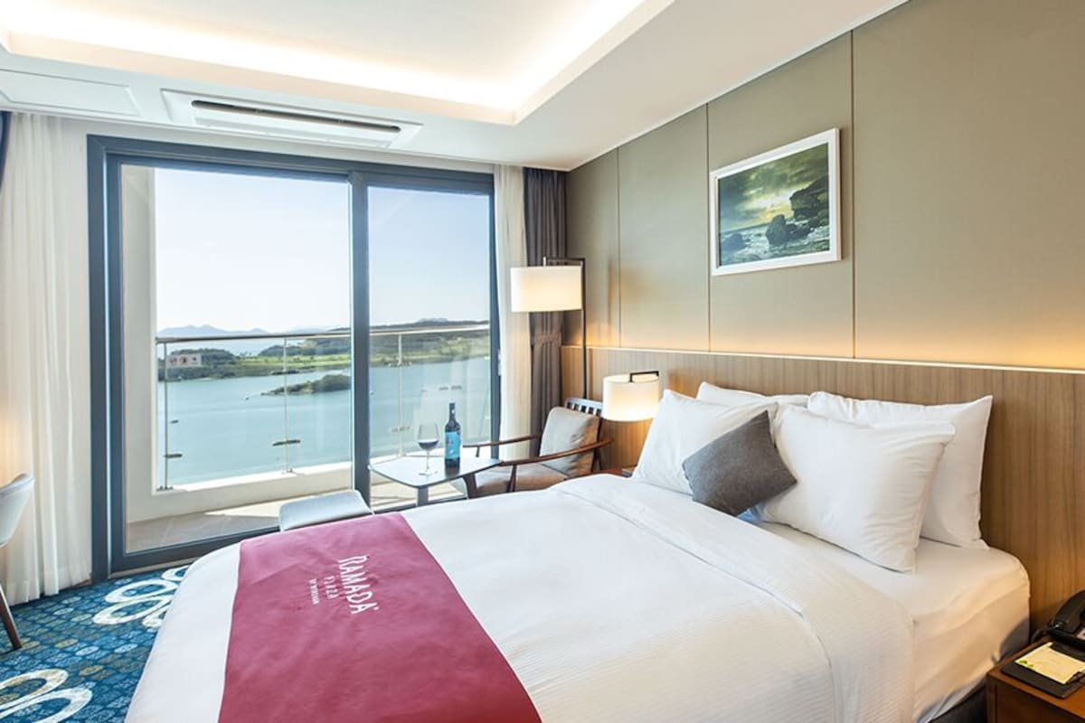 Habitación de hotel con una cama grande, un escritorio, una silla, una ventana con vista al mar y un cuadro en la pared.