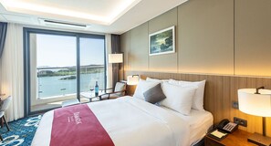 Quarto de hotel com uma cama grande, uma escrivaninha, uma cadeira, uma janela com vista para o mar e um quadro na parede.