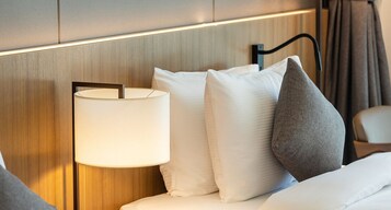 Una habitación de hotel con una cama, una lámpara de noche y un cabecero.