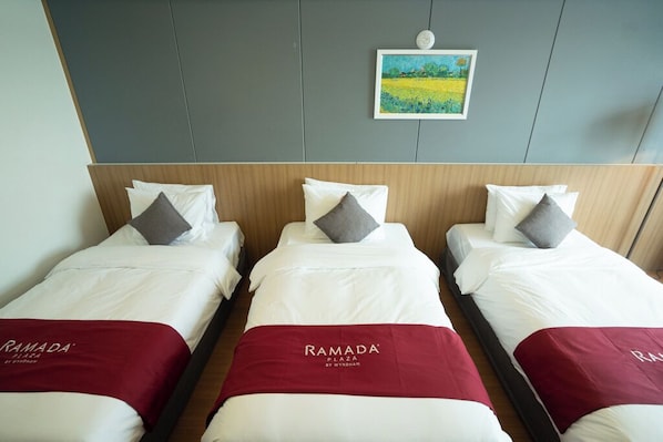 Three single beds with white bedding and red headboards, arranged in a row with a grey wall and a framed painting above. - Ramada Plaza by Wyndham Dolsan Yeosu (Yeosu)