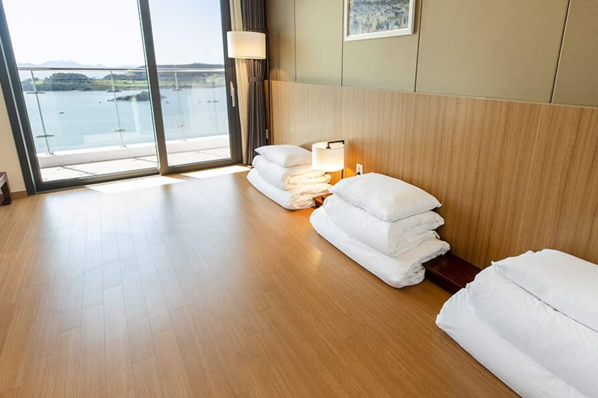 A hotel room with a large window, wooden floor, and a bed with white linens.