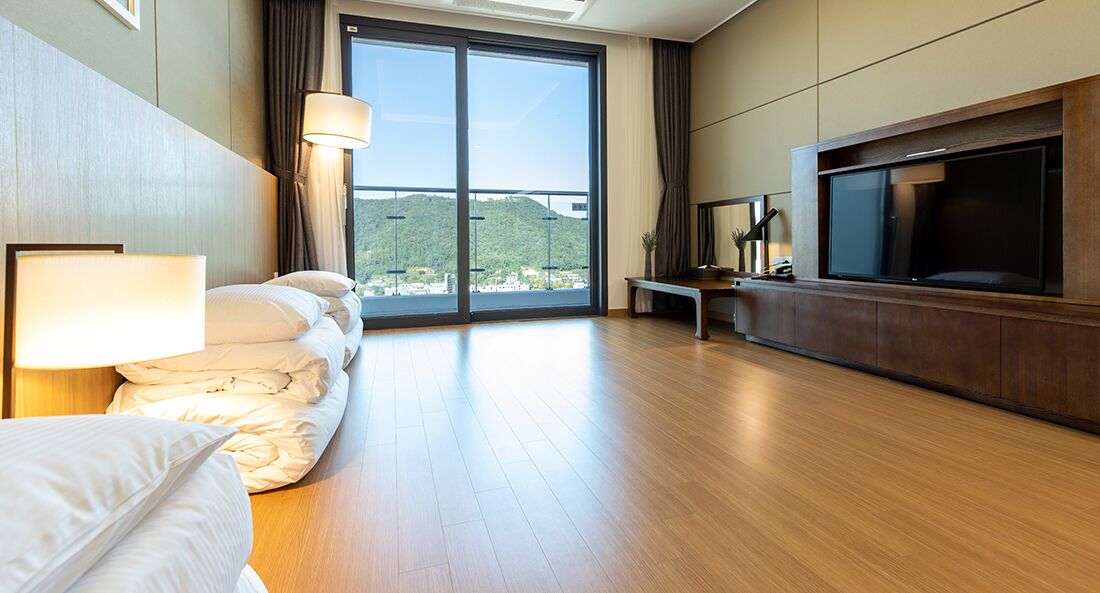 Ein modernes Hotelzimmer mit einem großen Bett, einem Fernseher und Blick auf eine Stadtkulisse durch raumhohe Fenster.