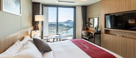 A hotel room with a large bed, a desk, a TV, and a balcony with a view of the landscape.