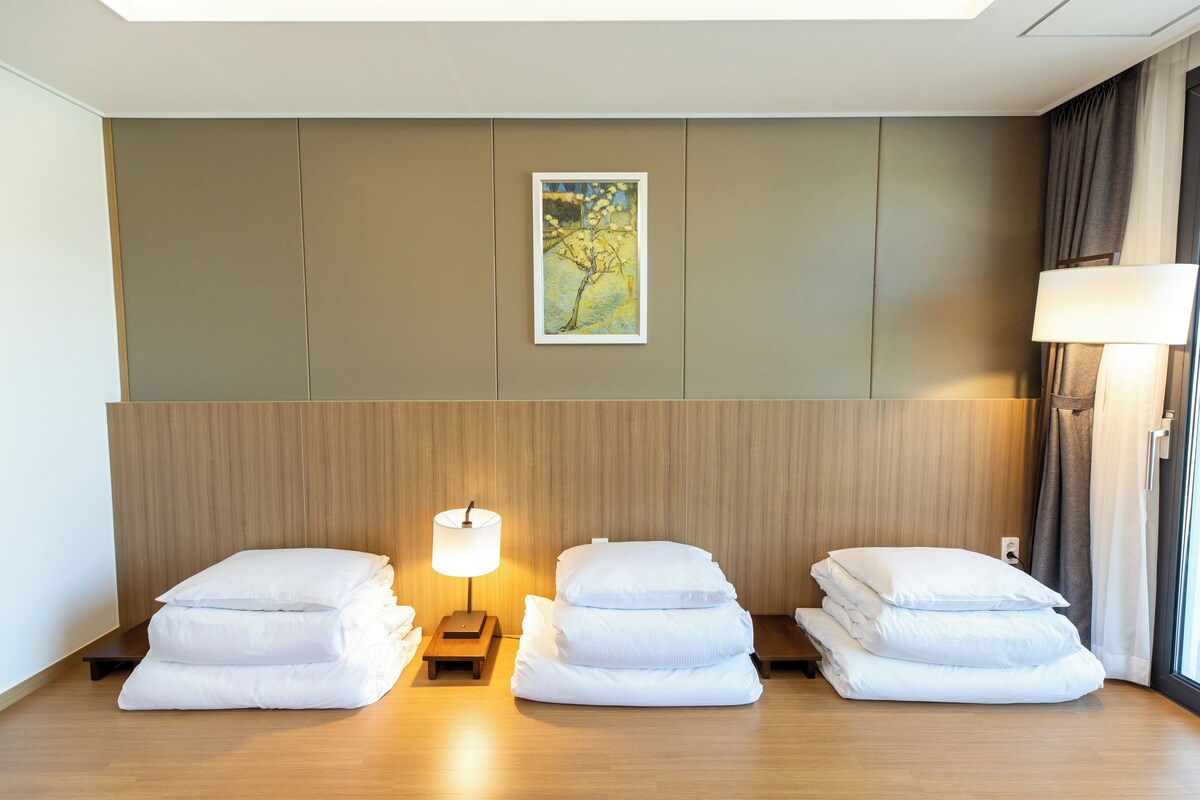 Habitación de hotel con cabecera de madera, un cuadro enmarcado, una lámpara de noche y almohadas ordenadas.