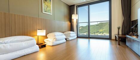 Habitación de hotel con una cama grande, un escritorio, una lámpara y vistas a una colina a través de un ventanal amplio.