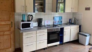 Una cocina compacta con armarios blancos, microondas, cafetera y cubo de basura.