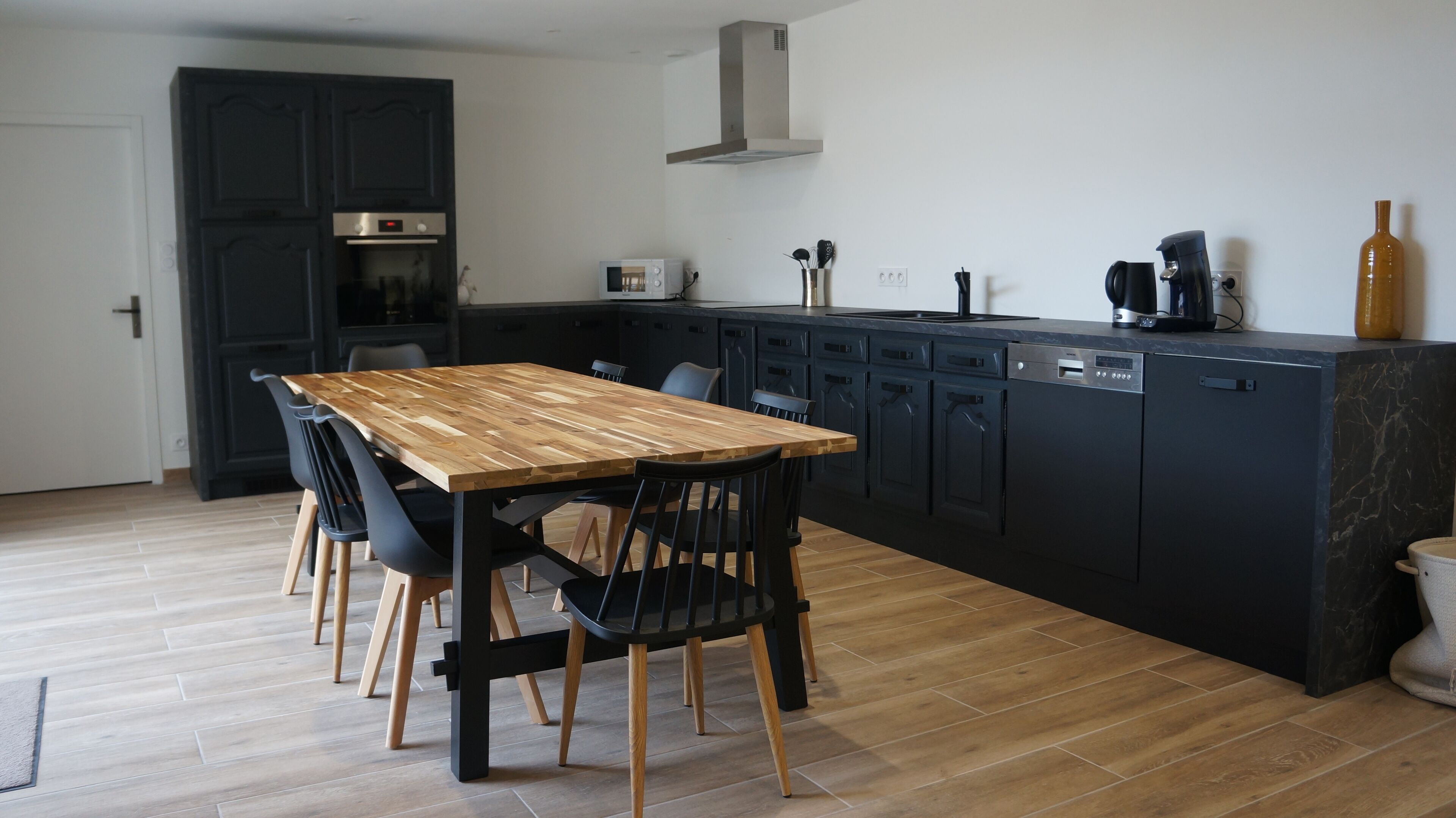 Une cuisine moderne avec une table et des chaises de salle à manger en bois, des meubles de rangement sombres et un four encastré.