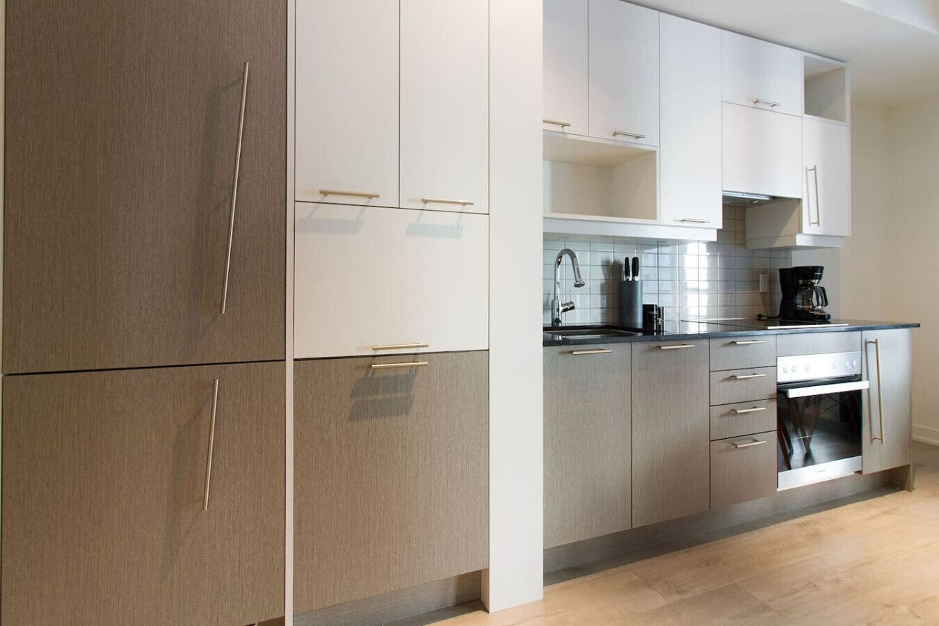 Una cocina moderna con gabinetes de madera clara, electrodomésticos de acero inoxidable y una cafetera negra sobre la encimera.