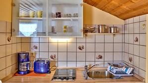 A compact kitchen with a wooden ceiling, a built-in cabinet with glass doors, a gas stove, a sink, and a coffee maker. - Ferienwohnungen Wirth (Bodenmais)