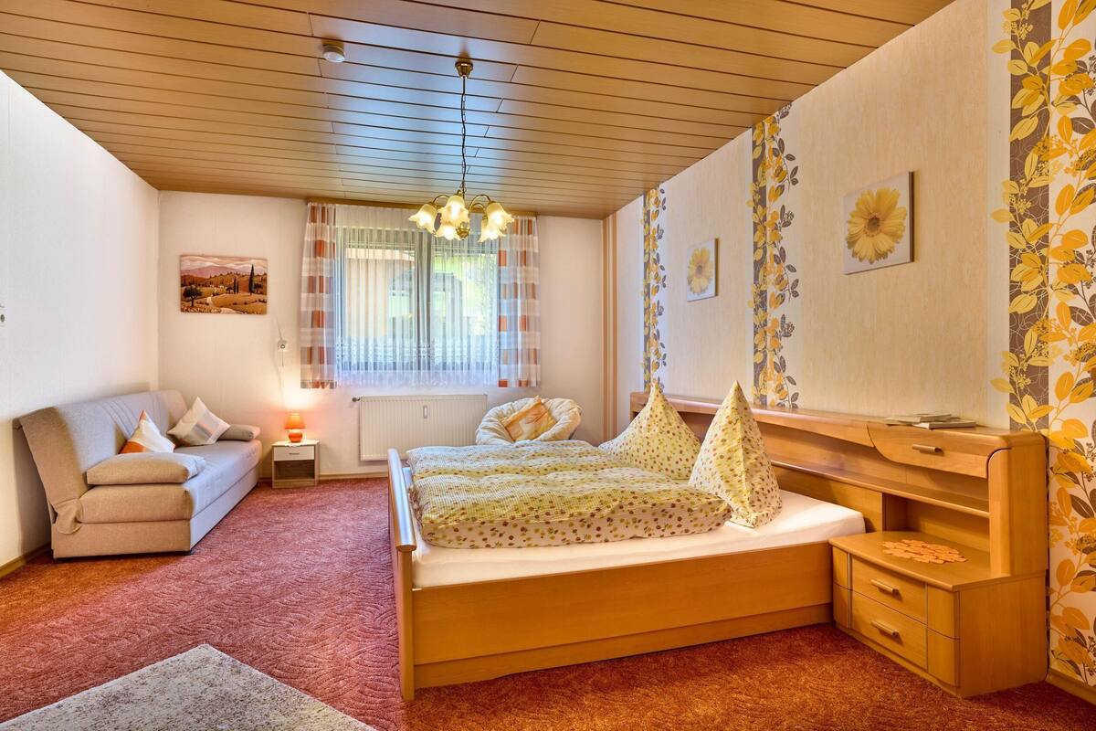 A bedroom with a wooden bed, a sofa, a desk, and a window with curtains.