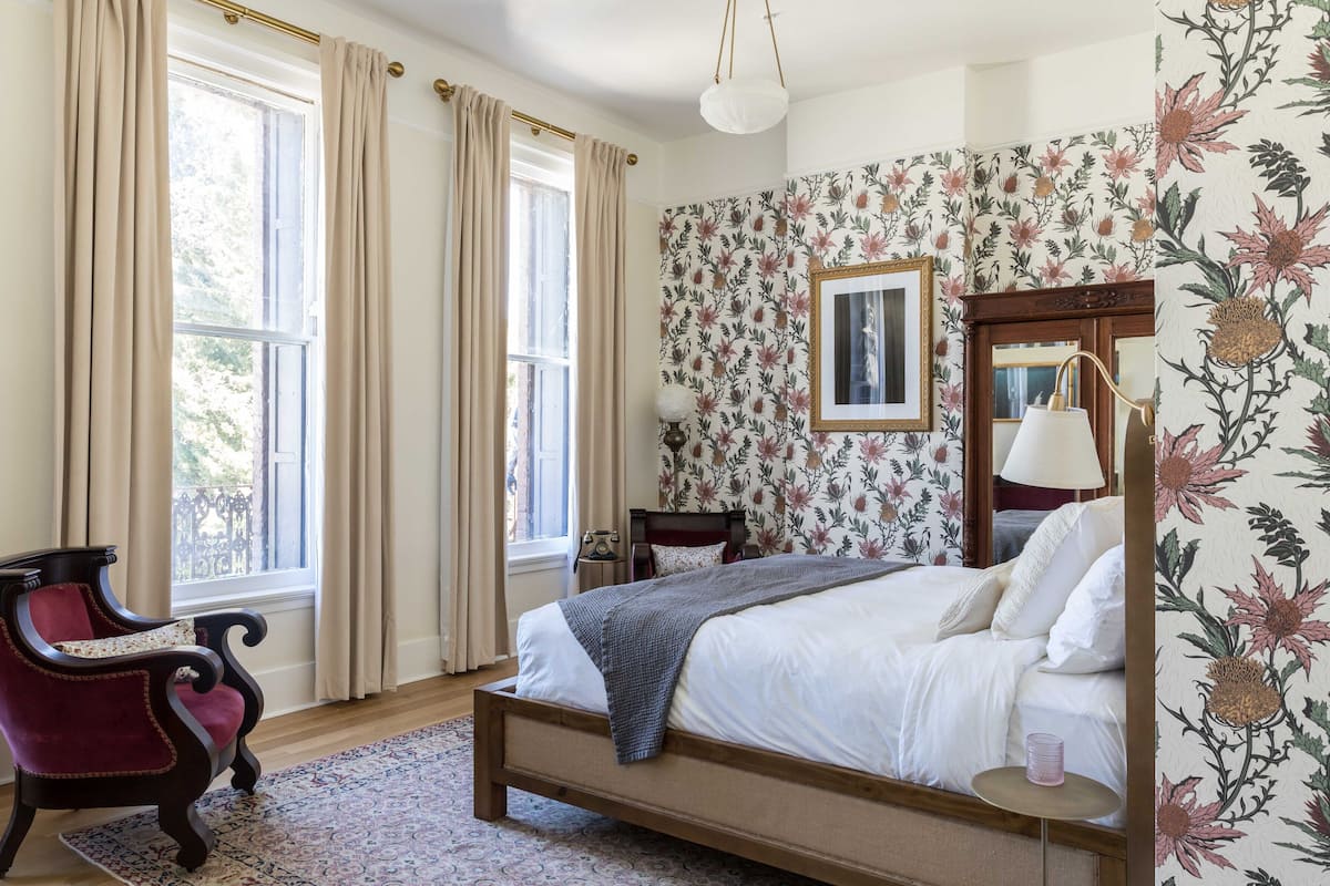 A bedroom with a large bed, a chair, a nightstand, and a window with curtains.