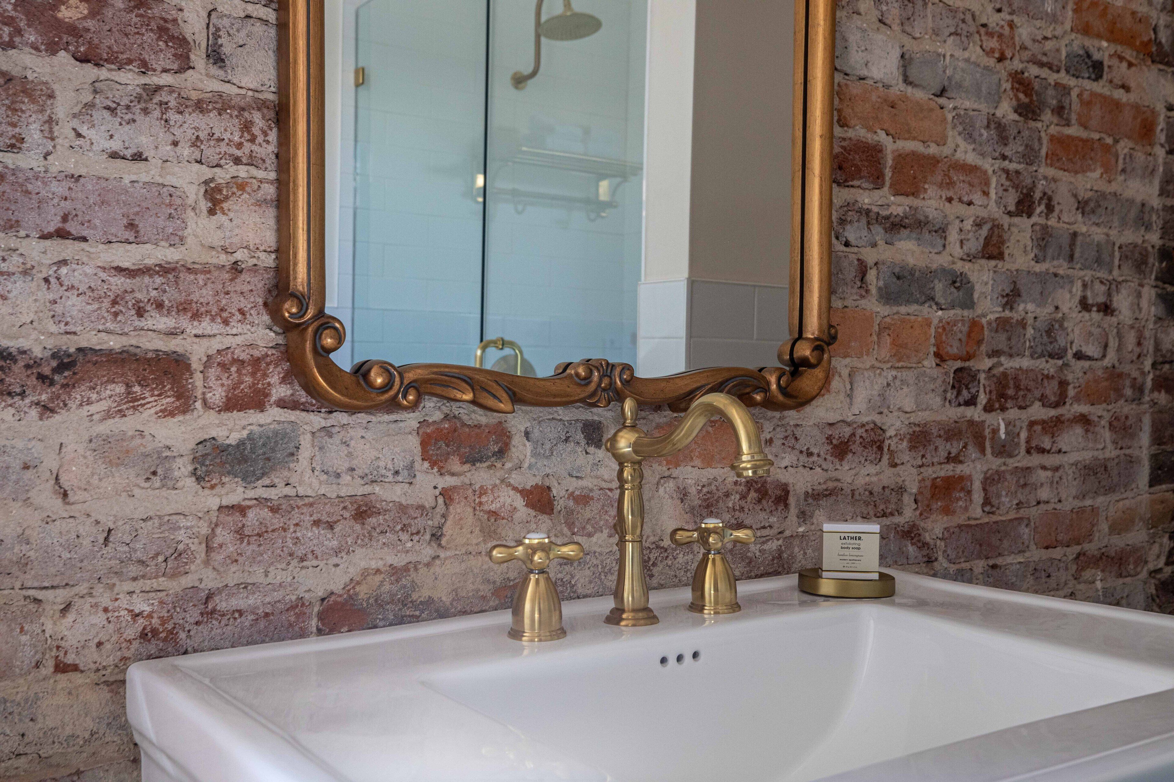 A bathroom with a white sink, gold faucets, and a mirror with an ornate frame.