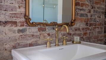 A bathroom with a white sink, gold faucets, and a mirror with an ornate frame.