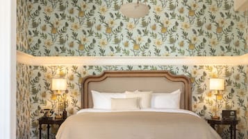 A bedroom with a large bed, two bedside tables with lamps, a hanging light fixture, and floral wallpaper.