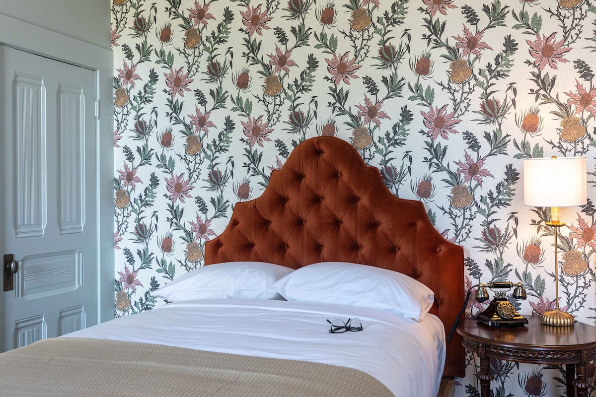 A neatly made bed with white linens, a tufted headboard, and a bedside table with a lamp.