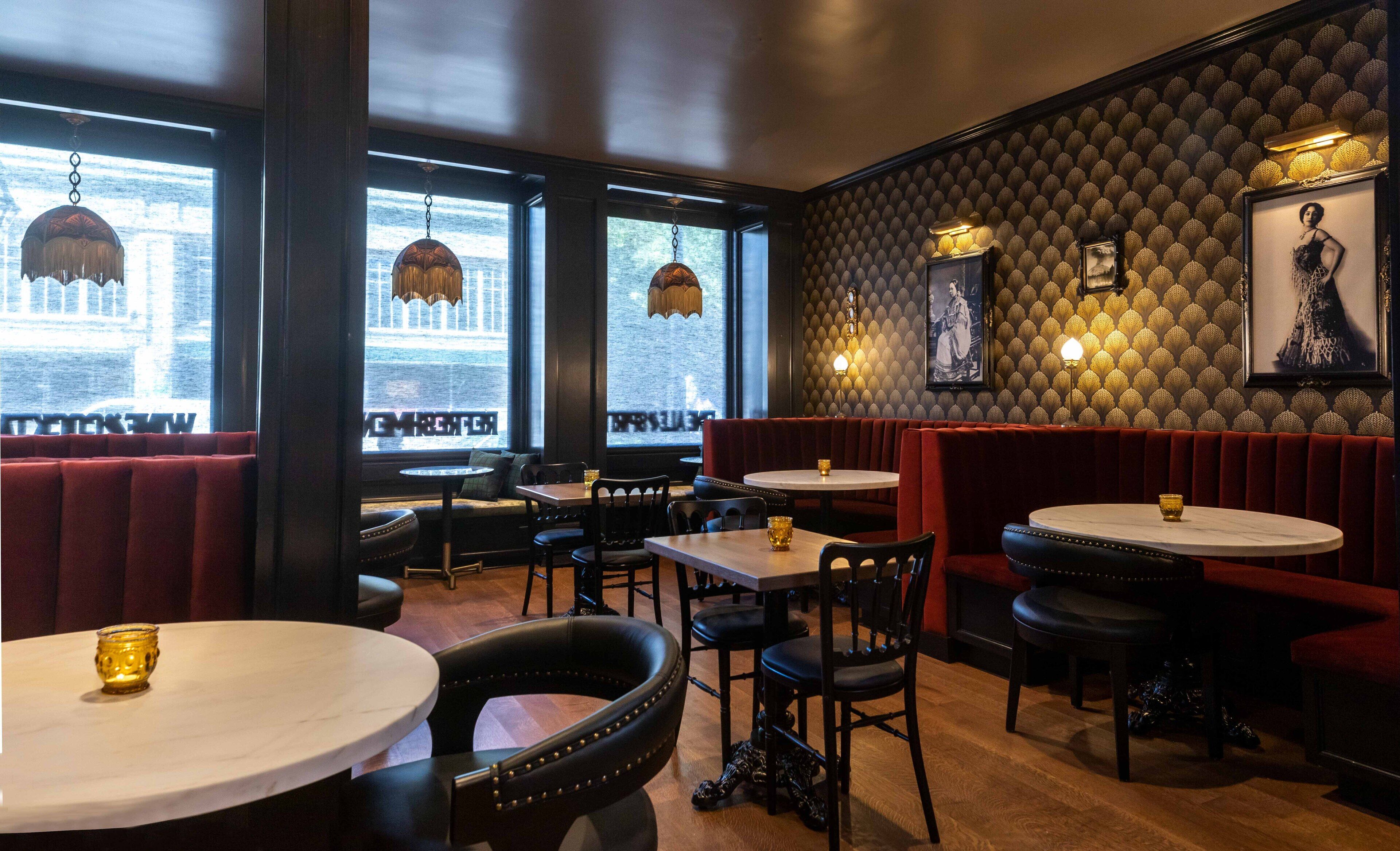 Un interior de restaurante con cabinas, mesas redondas y lámparas colgantes.