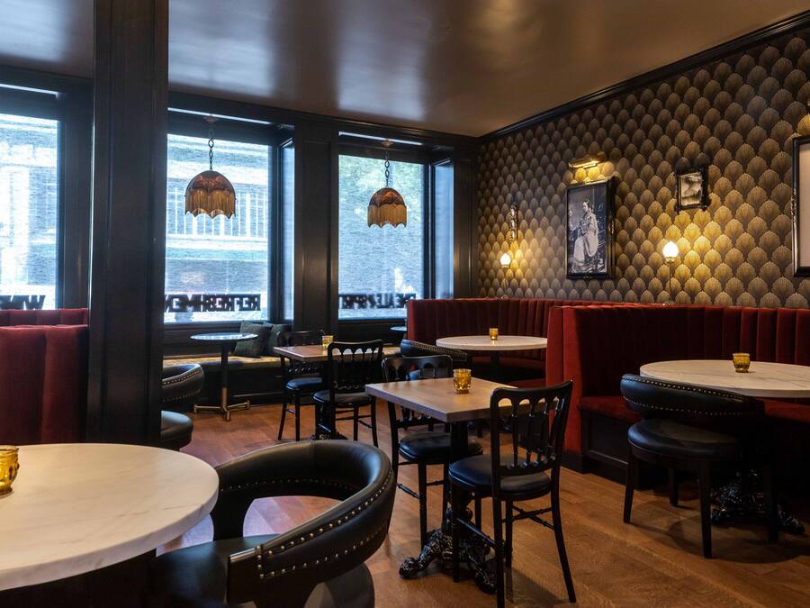 Un interior de restaurante con cabinas, mesas redondas y lámparas colgantes.