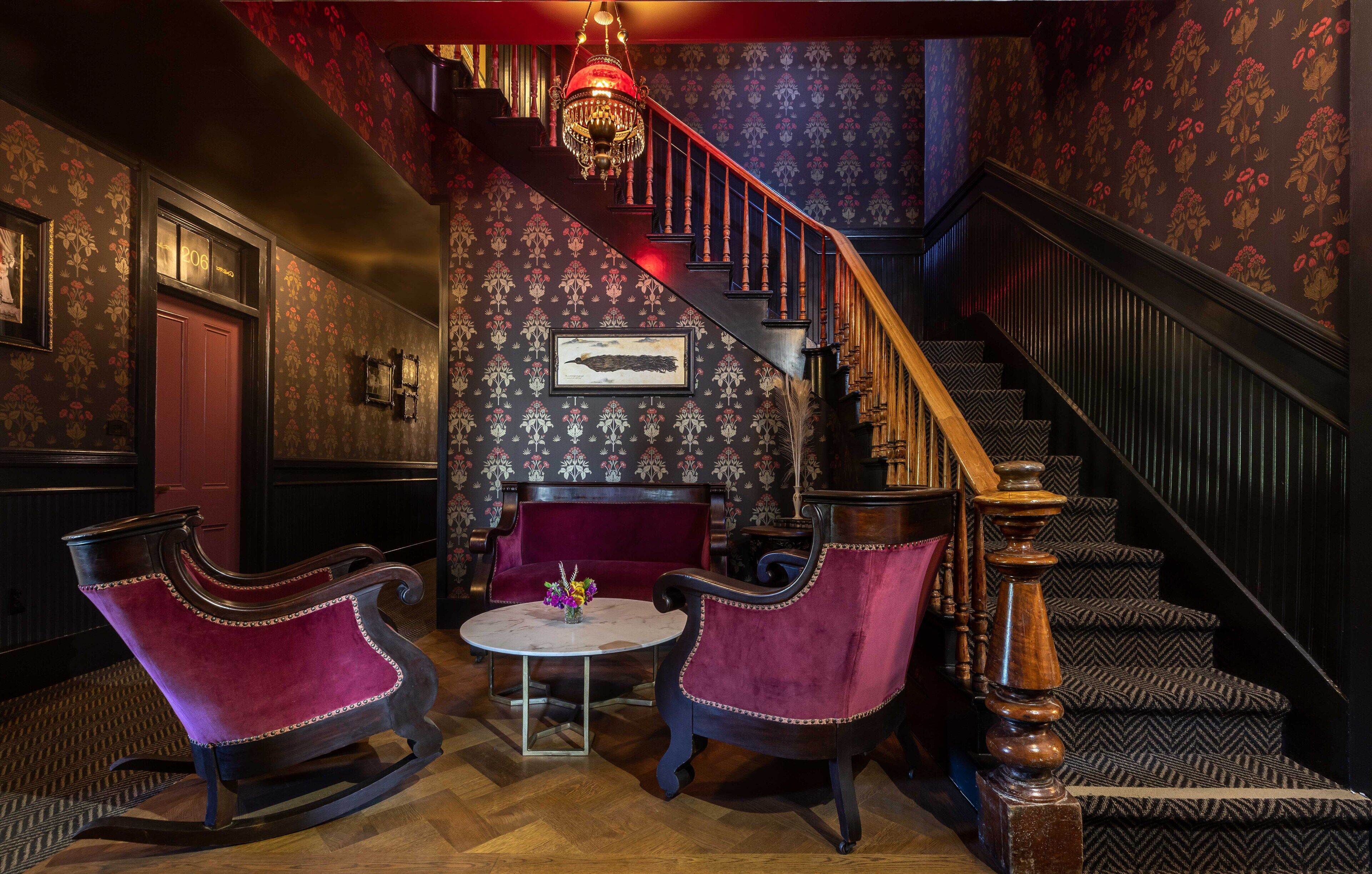 A grand staircase with ornate railings, a red velvet sofa, and a chandelier.