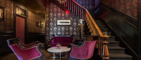 A grand staircase with ornate railings, a red velvet sofa, and a chandelier.