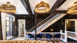 Een statige trap met een witte balustrade, een sofa met gestuikt leer en een kroonluchter.