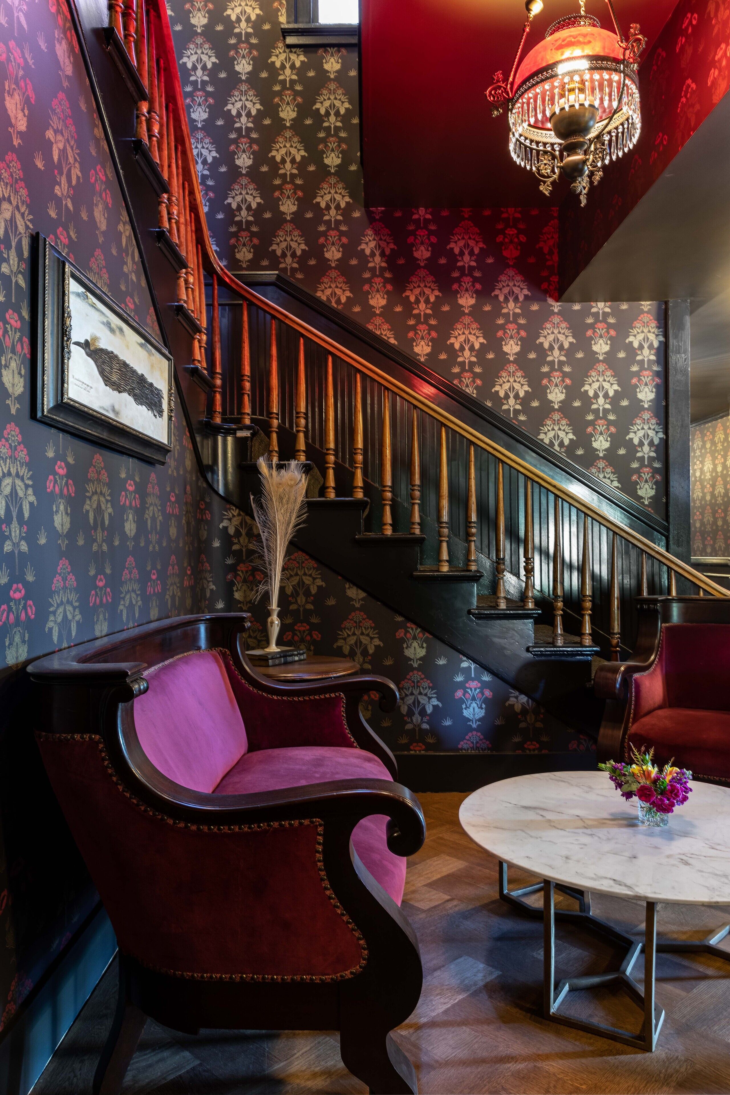 A staircase with ornate railings, a chandelier, and patterned wallpaper.