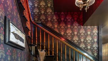 A staircase with ornate railings, a chandelier, and patterned wallpaper.