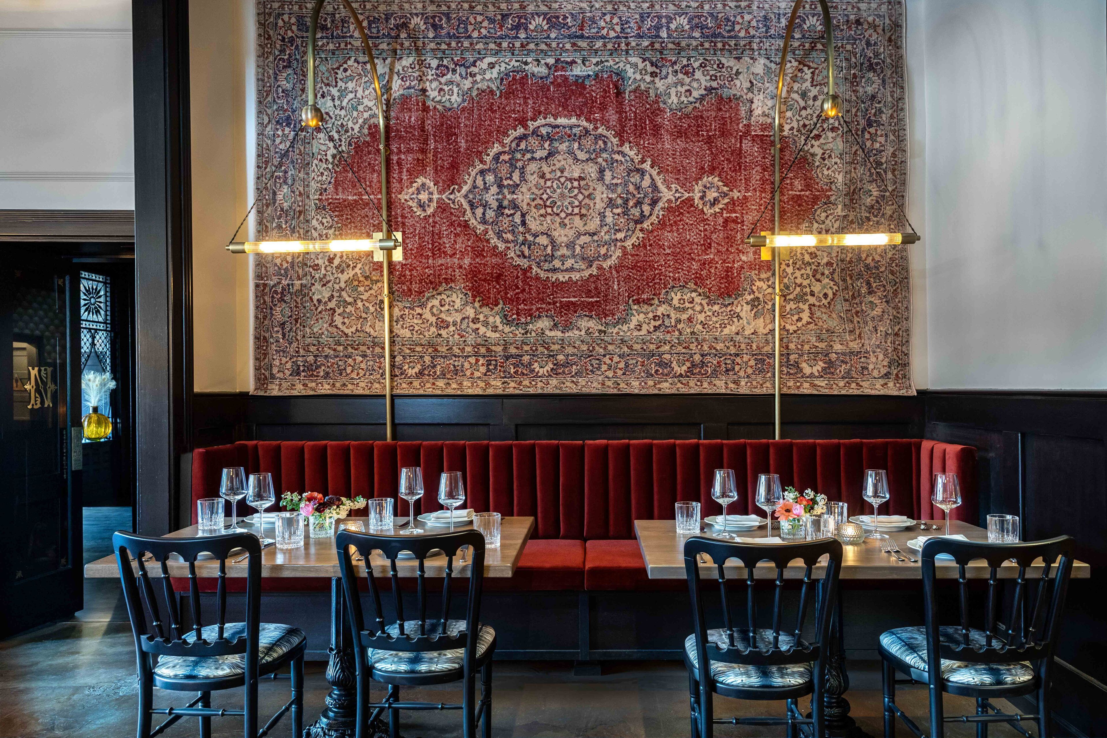 A restaurant with a red upholstered booth, wooden tables, and black chairs.