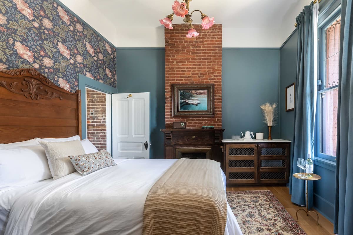 A bedroom with a bed, a fireplace, a dresser, a door, and a window with curtains.