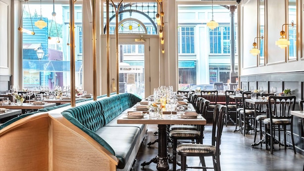 Een restaurant met een lange toonbank, een groen bekleden bankje en een hoge plafond met zichtbare balken.