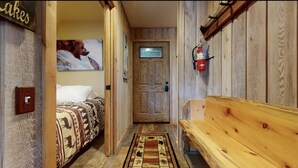 Un pasillo estrecho con un banco de madera, una cama con ropa de cama estampada, un extintor y una puerta con un panel de vidrio esmerilado.