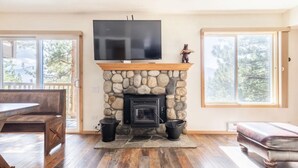 Una sala de estar con chimenea de piedra, un televisor montado encima y un ventanal grande a un lado.