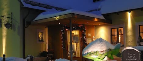 A building with a snow-covered entrance, a sign with text, and a small garden area with a snowman.