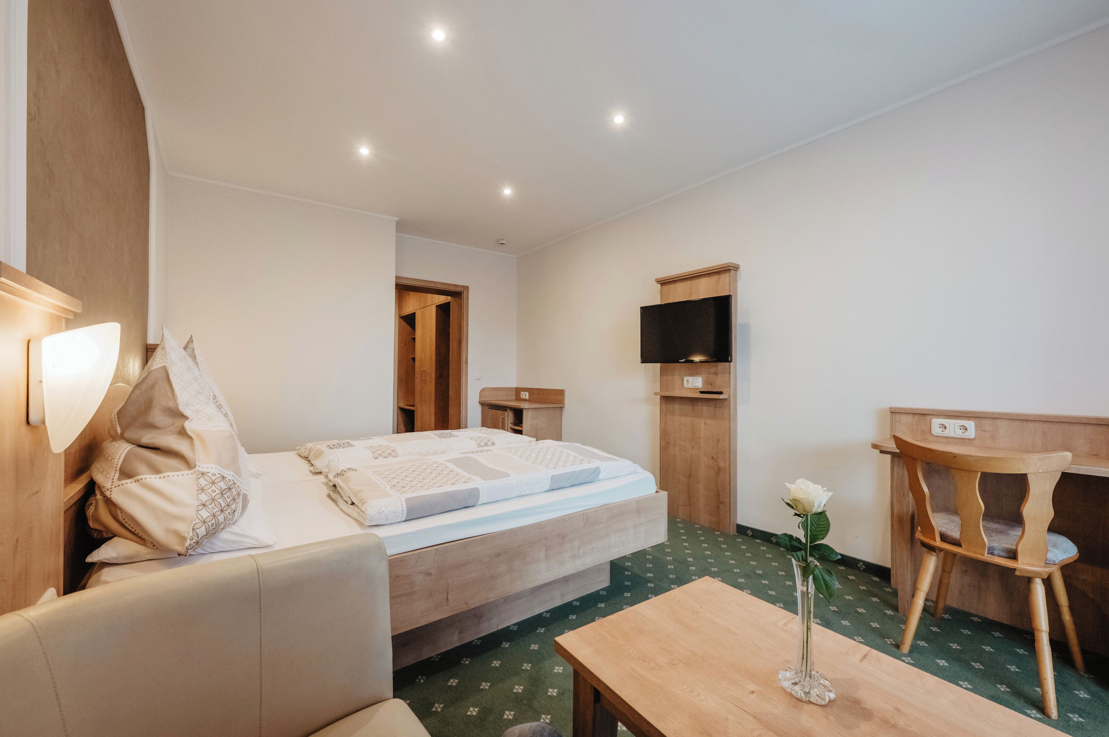 Een hotelkamer met een bed, een bureau, een stoel, een televisie en een vaas met een bloem.