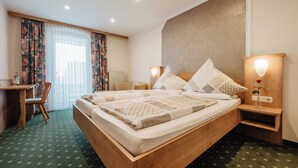 A hotel room with a wooden bed, a desk, a chair, a nightstand with a lamp, and a window with curtains. - Gasthof-Metzgerei-Pension Schierlitz (Rimbach)