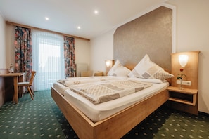 A hotel room with a wooden bed, a desk, a chair, a nightstand with a lamp, and a window with curtains. - Gasthof-Metzgerei-Pension Schierlitz (Rimbach)