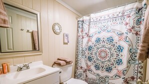 Une salle de bain équipée d’un lavabo, d’un miroir, de toilettes et d’un rideau de douche à motifs.