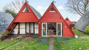 Una cabaña tipo A de color rojo con un espacio central para la sala, un porche cubierto y un pequeño jardín.