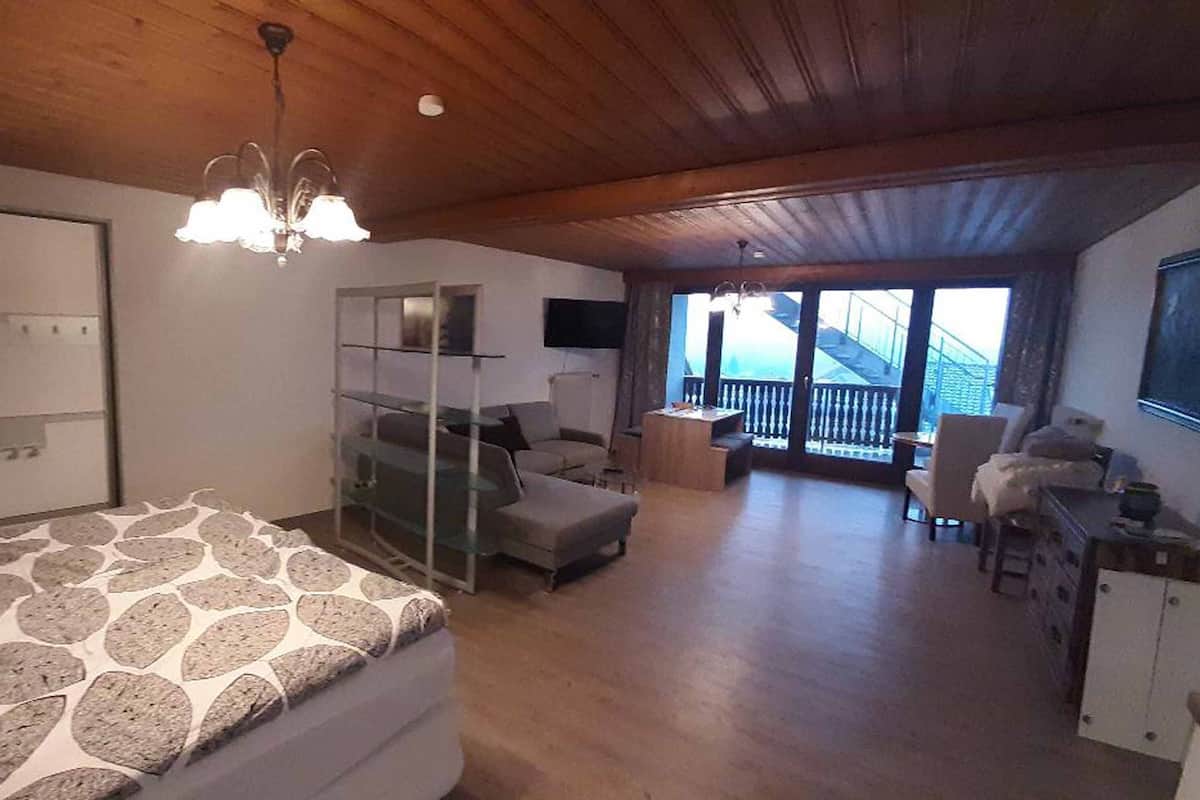 A spacious room with a large bed, a desk, and a balcony with a view.