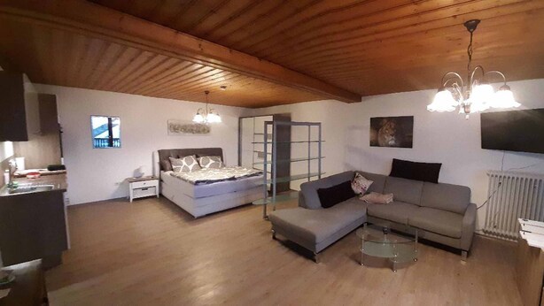 A spacious living area with a bed, sofa, and a TV mounted on the wall. - Haus Naturenergie (Frauenau)