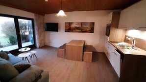 A modern kitchen with wooden cabinets, a dining area with a table and chairs, and a large window providing a view of the outdoors. - Haus Naturenergie (Frauenau)