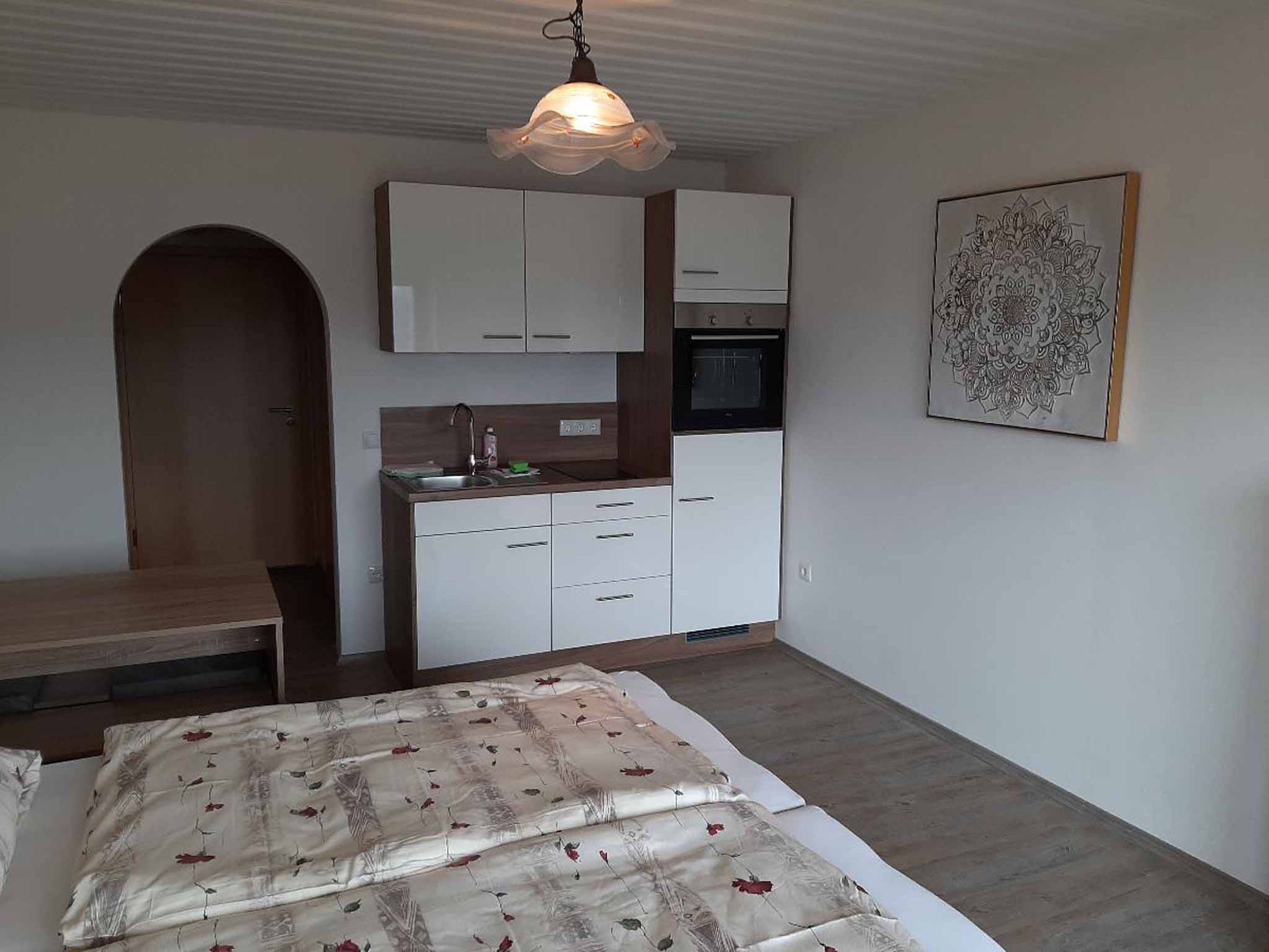 A compact bedroom with a bed, a small kitchenette, and a door leading to another room.