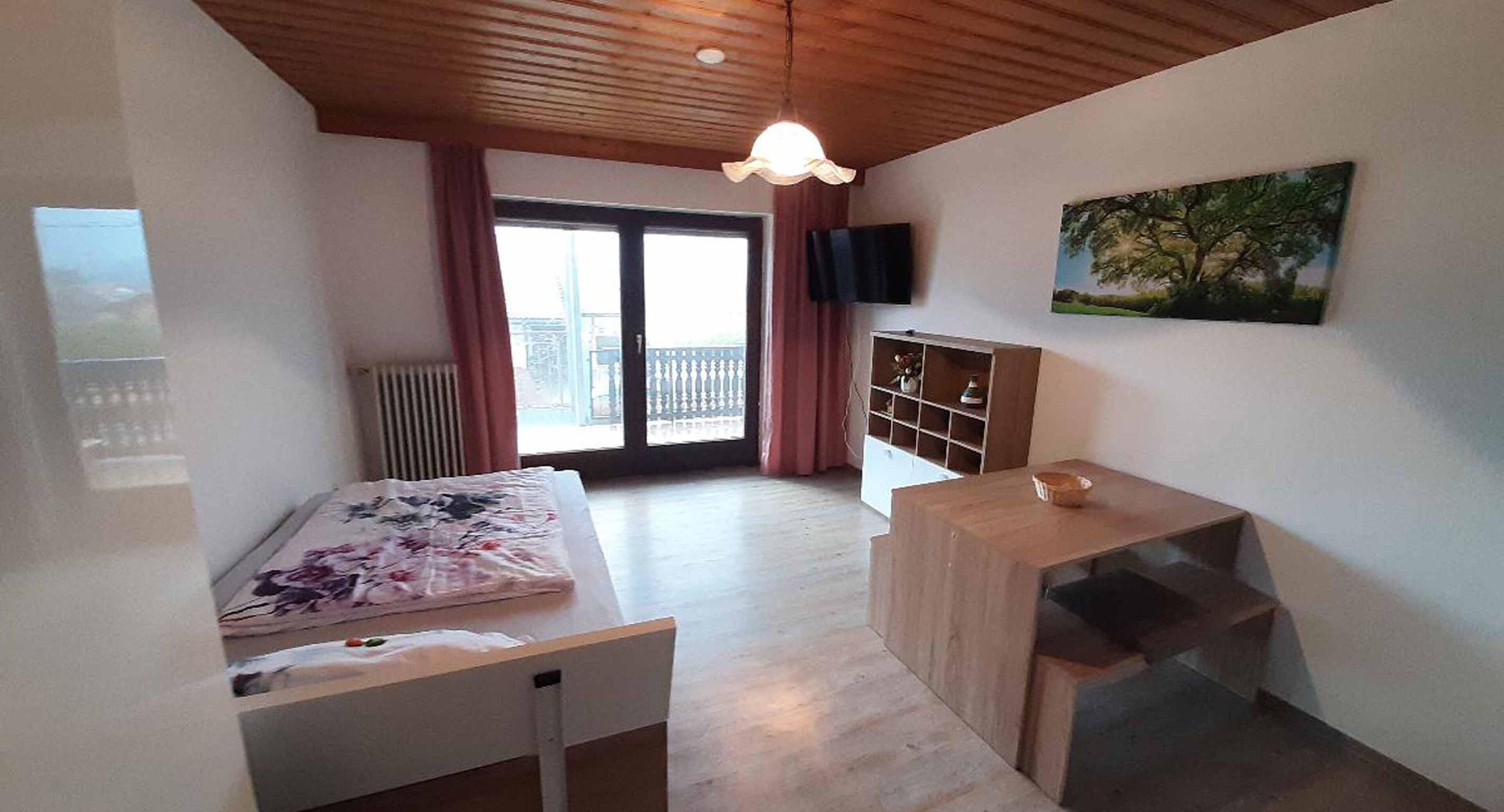 Un dormitorio con cama, un escritorio de madera, un televisor y un cuadro en la pared.