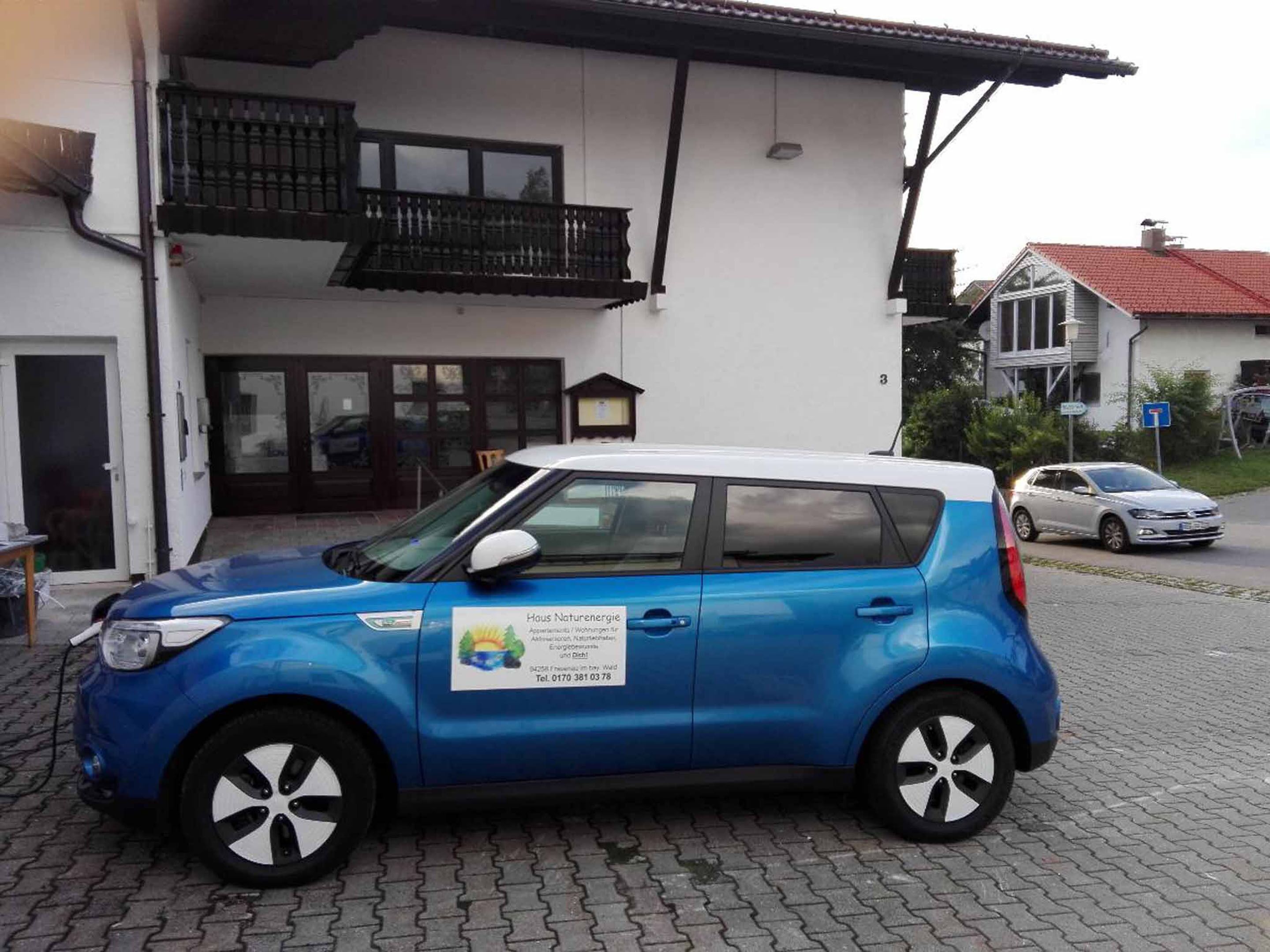 A blue car parked in front of a building with a balcony.