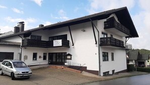A two-story building with a white facade, multiple balconies, and a car parked in front. - Haus Naturenergie (Frauenau)