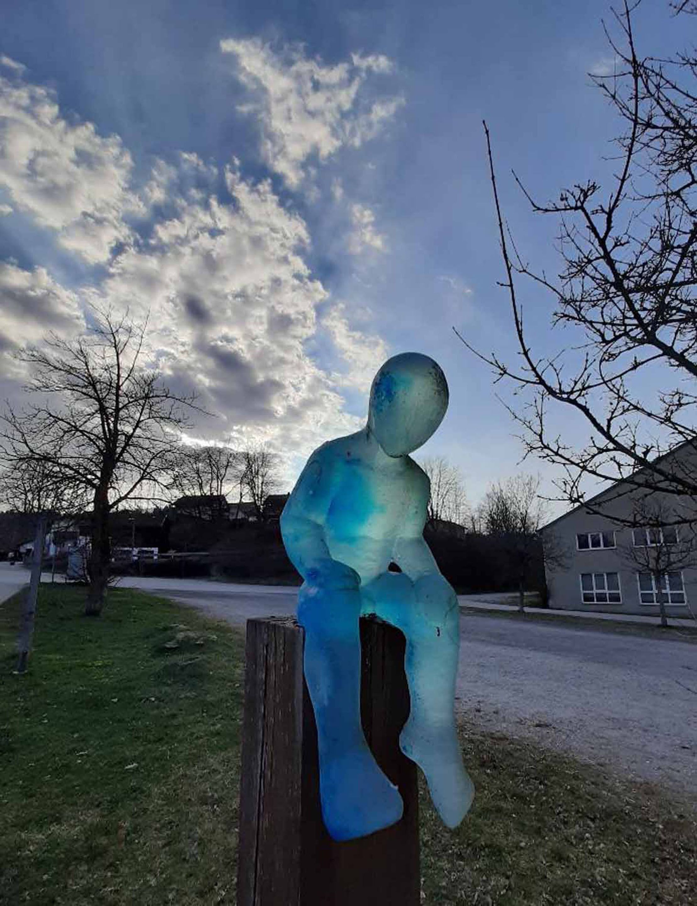 A sculpture of a human figure sitting on a wooden post.