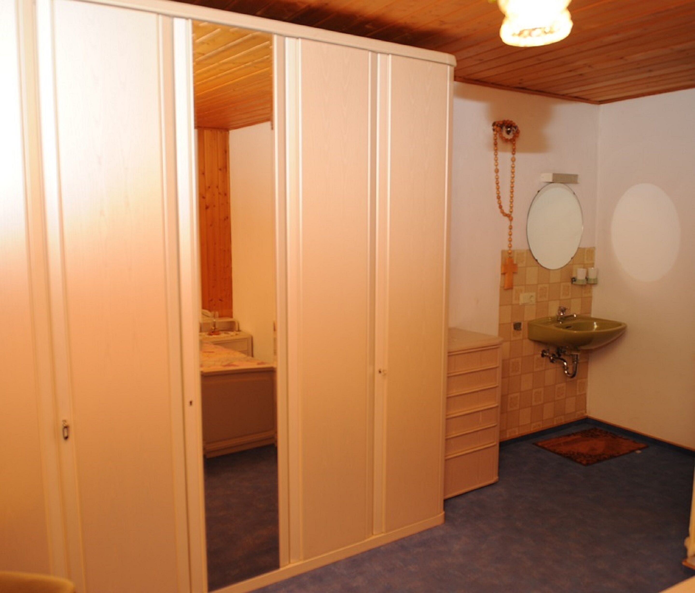 Een slaapkamer met een houten garderobe, een kleine badkamer met een wastafel en spiegel, en een vloerbedekking.