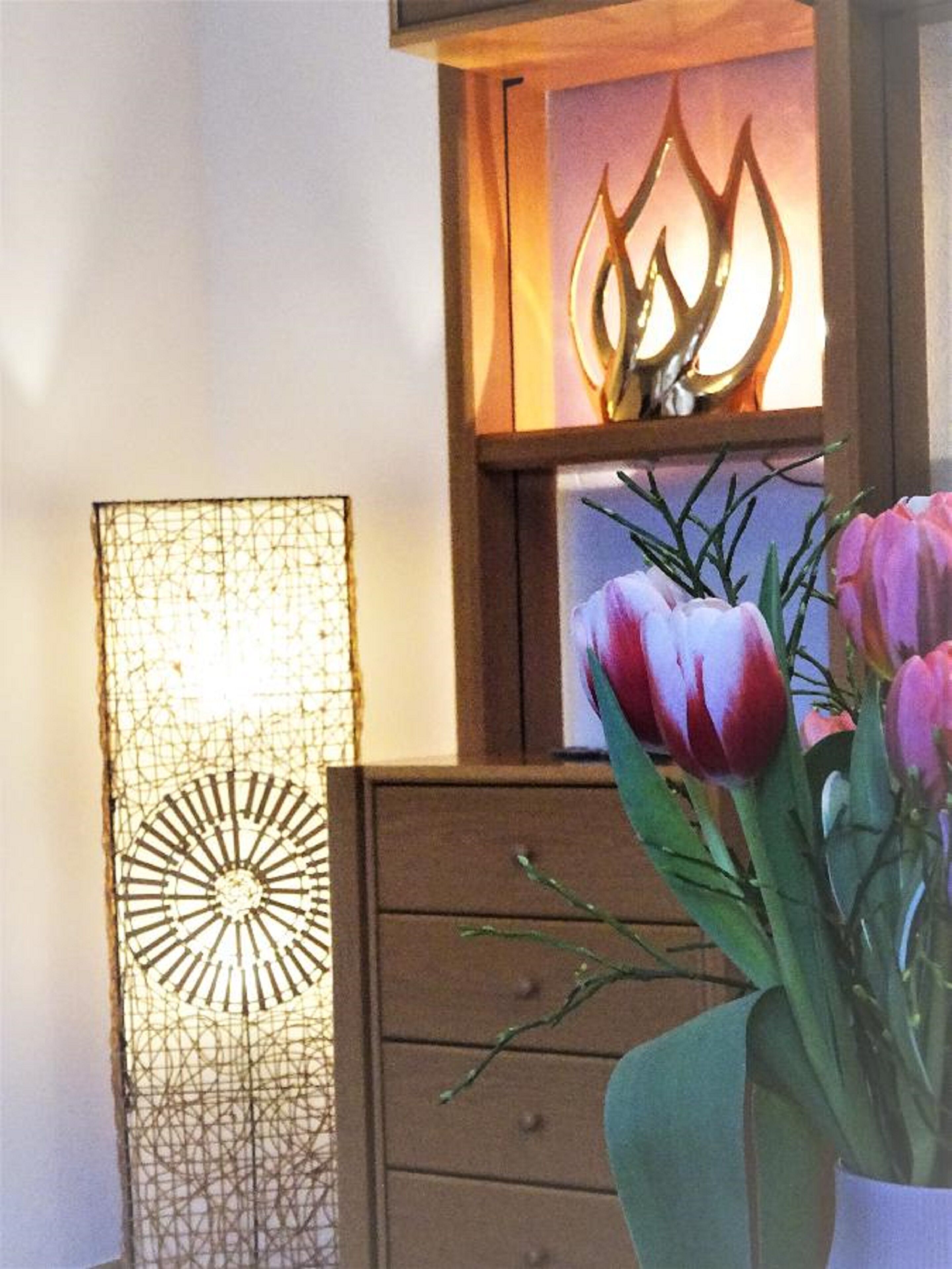 A wooden cabinet with a decorative glass panel, a wall-mounted light fixture, and a vase with pink tulips.