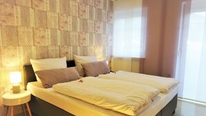 Una habitación de hotel moderna con una cama grande, una mesita de noche con lámpara y un papel tapiz estampado en la pared.