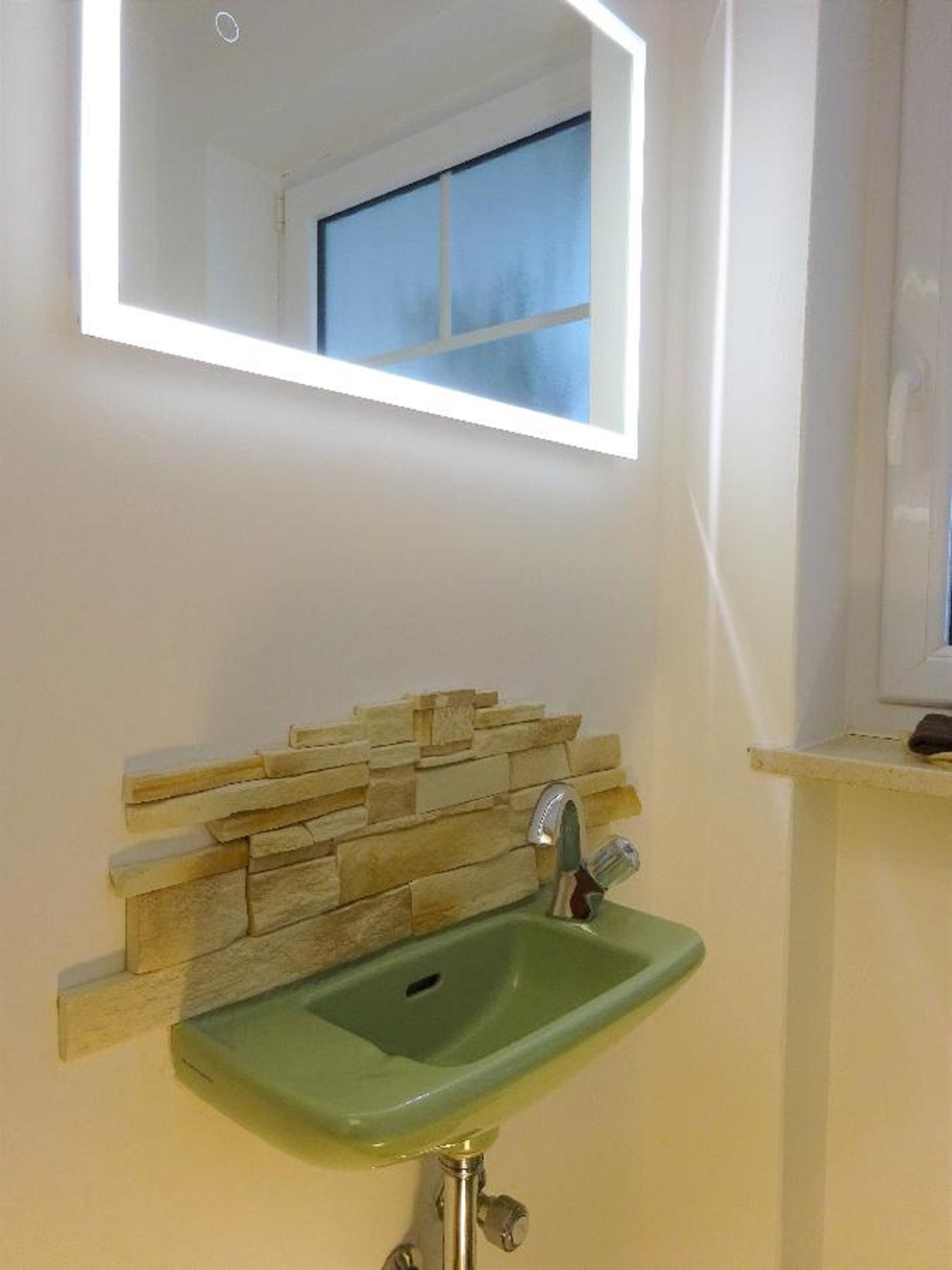 Un baño con un lavabo verde, un salpicadero de piedra y un espejo encima.