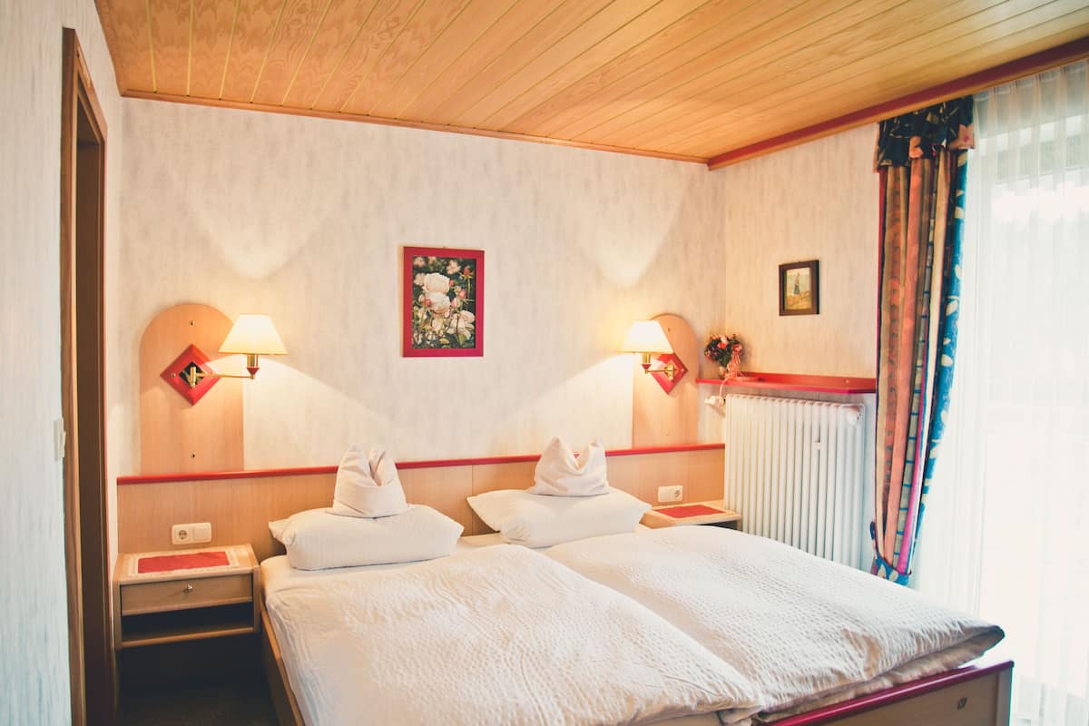 A hotel room with two beds, a wooden ceiling, a radiator, and two wall-mounted lamps.